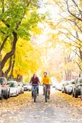 Two 学生 ride down Greek Row in the fall, amid changing leaves.